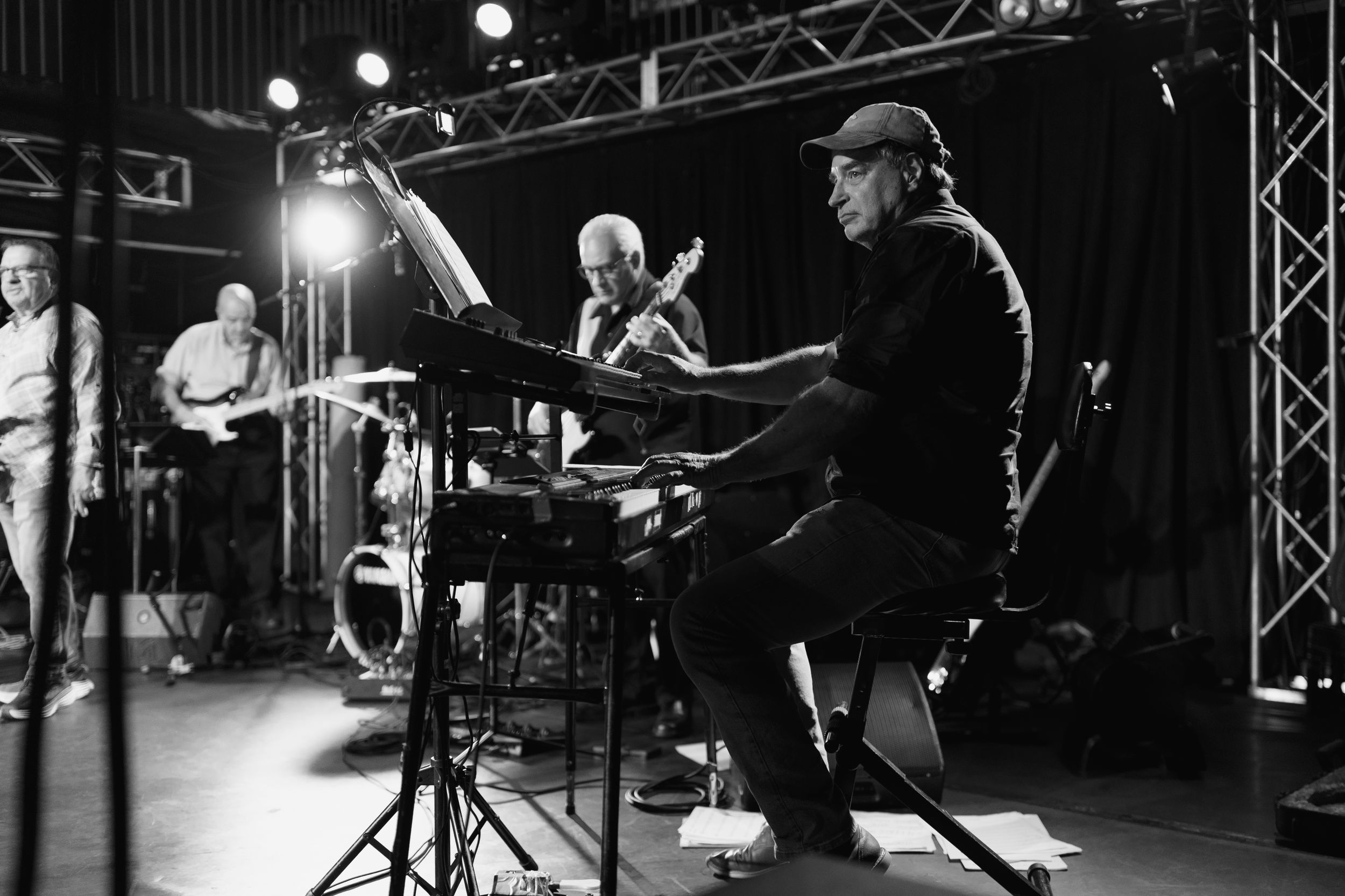 Musicians performing on stage with lighting rigs and sound equipment visible in a black and white concert photograph.
