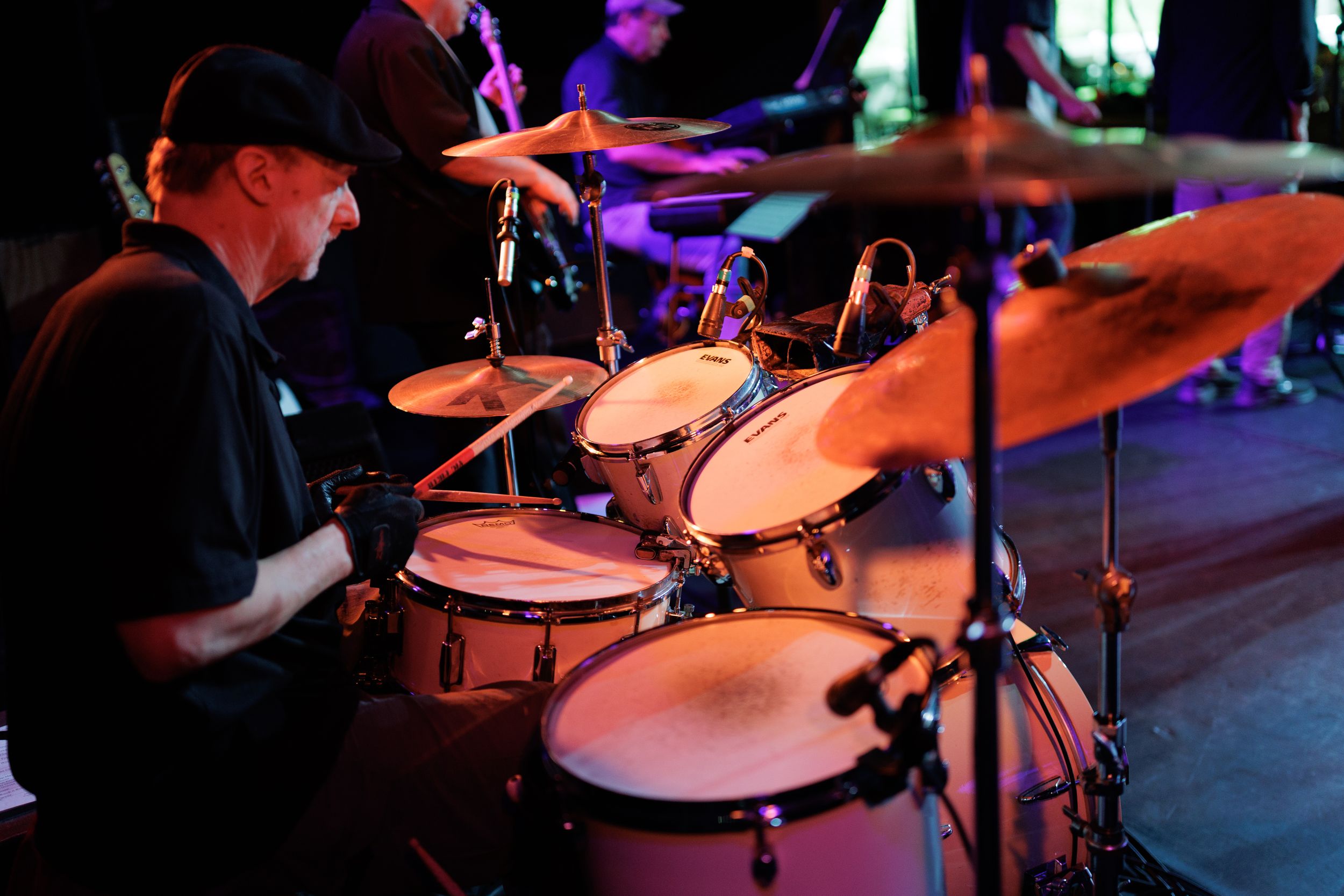 Professional drummer performs on stage playing a drum kit under purple stage lighting during a live performance event.