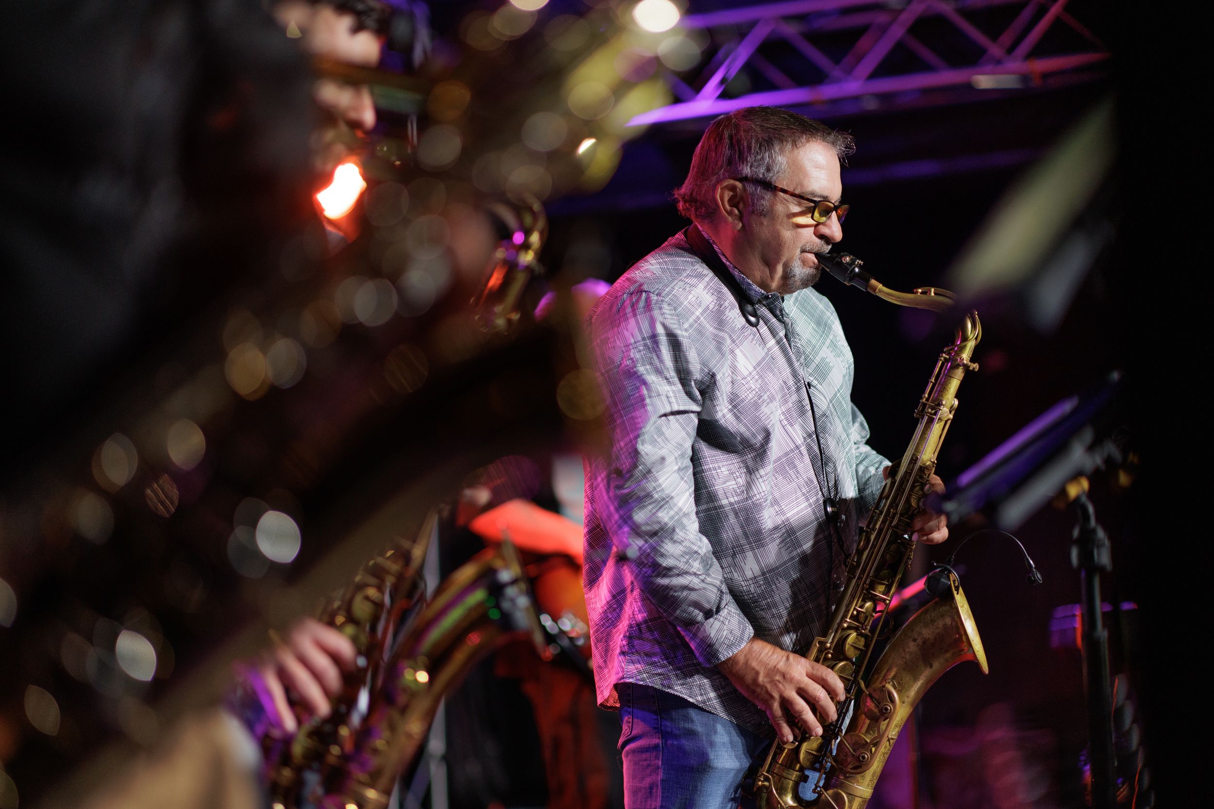 Saxophone player performs on stage with colorful purple lighting and bokeh effects in the background.