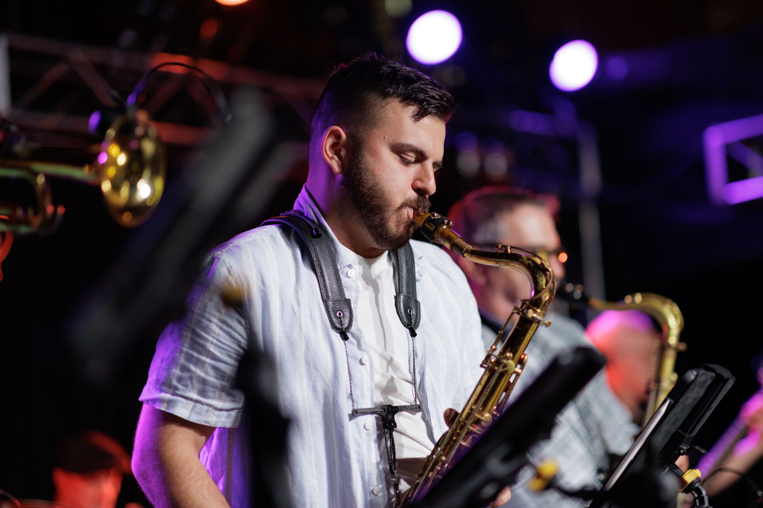 Musicians perform on stage with saxophones under purple stage lighting at a nightclub venue.