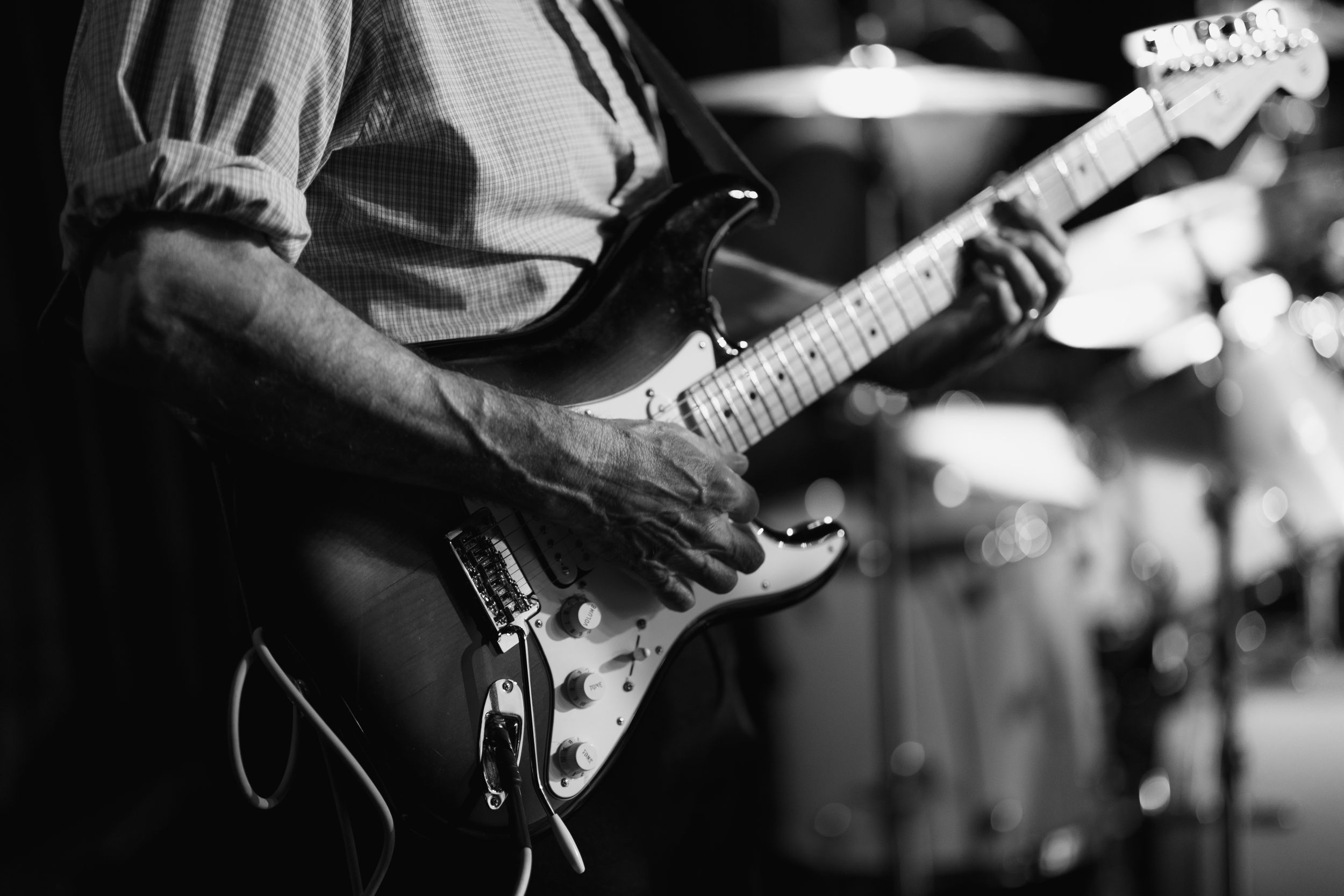 Black and white photo of musician playing electric guitar during live performance with blurry stage lights in background.
