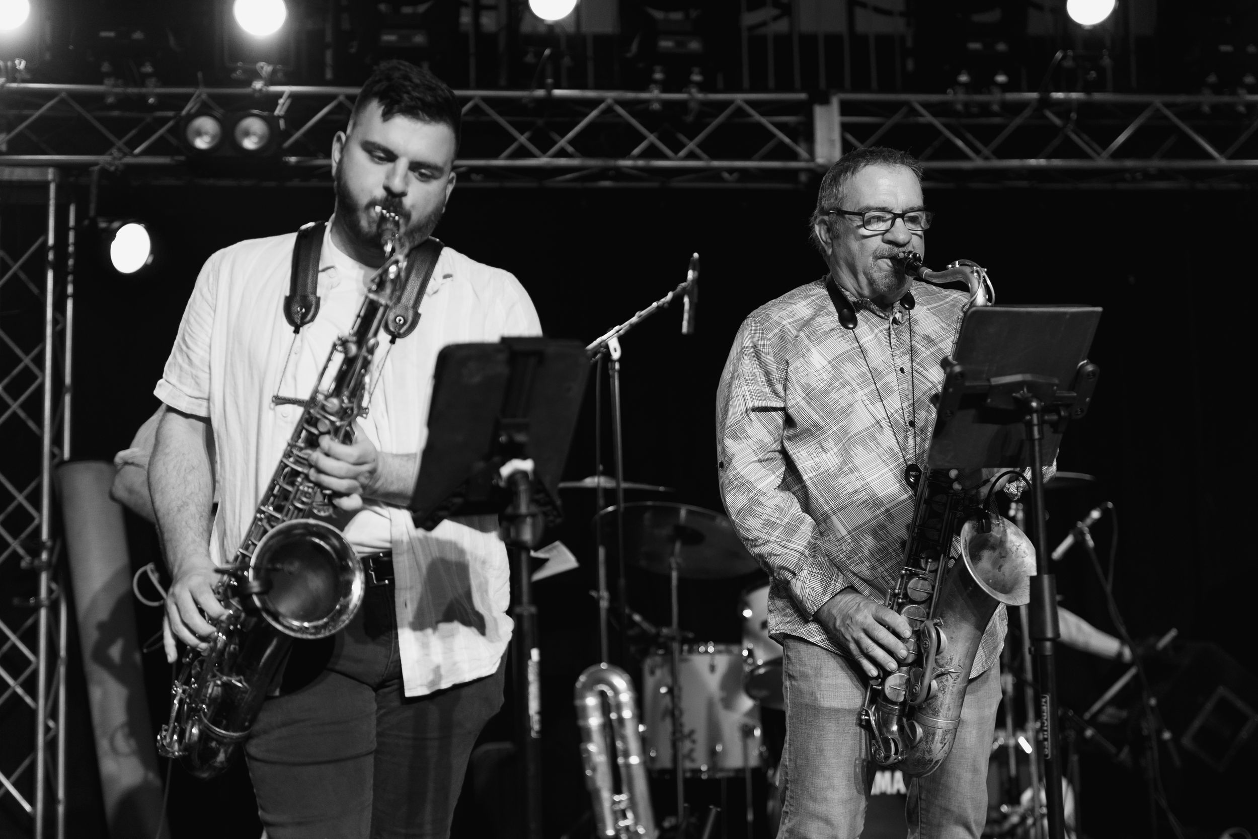 Two saxophone players performing together in black and white at a live music show.