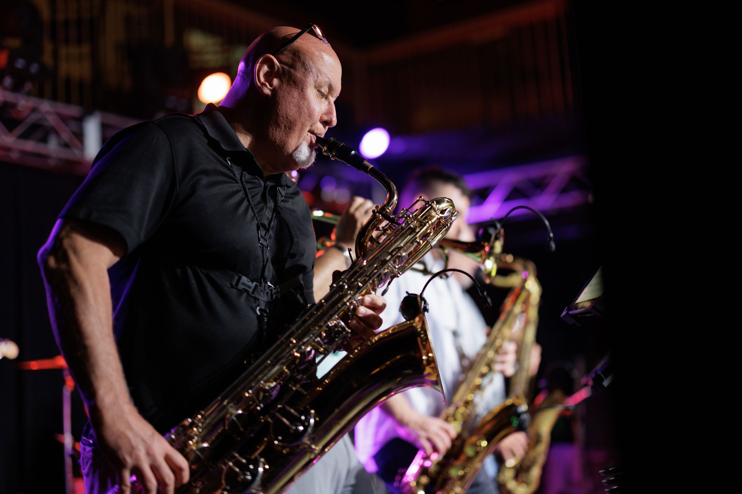 Musician playing saxophone on stage with dramatic purple lighting creates atmospheric performance vibes.