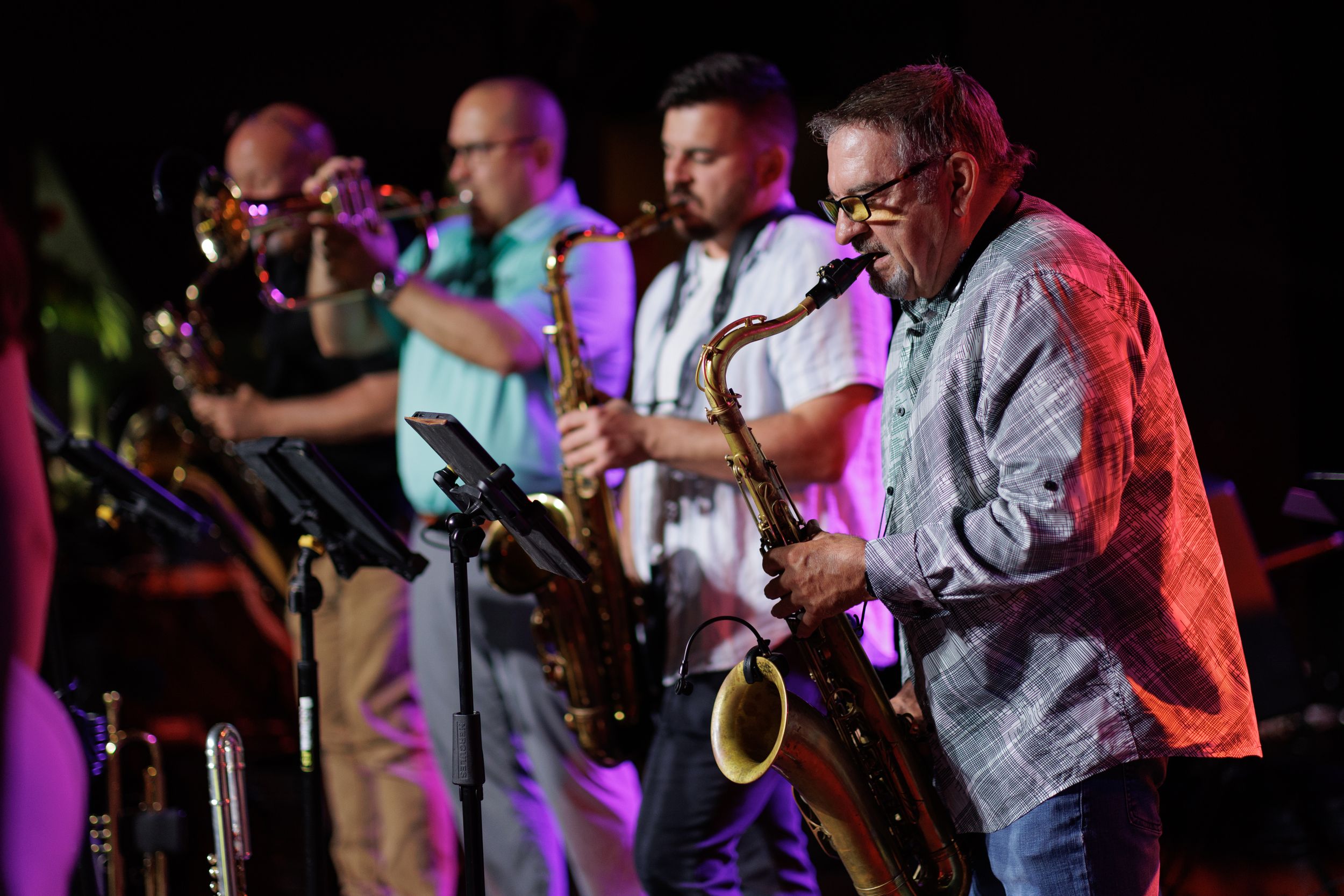 Jazz musicians perform on stage with saxophones and instruments under colorful stage lighting.
