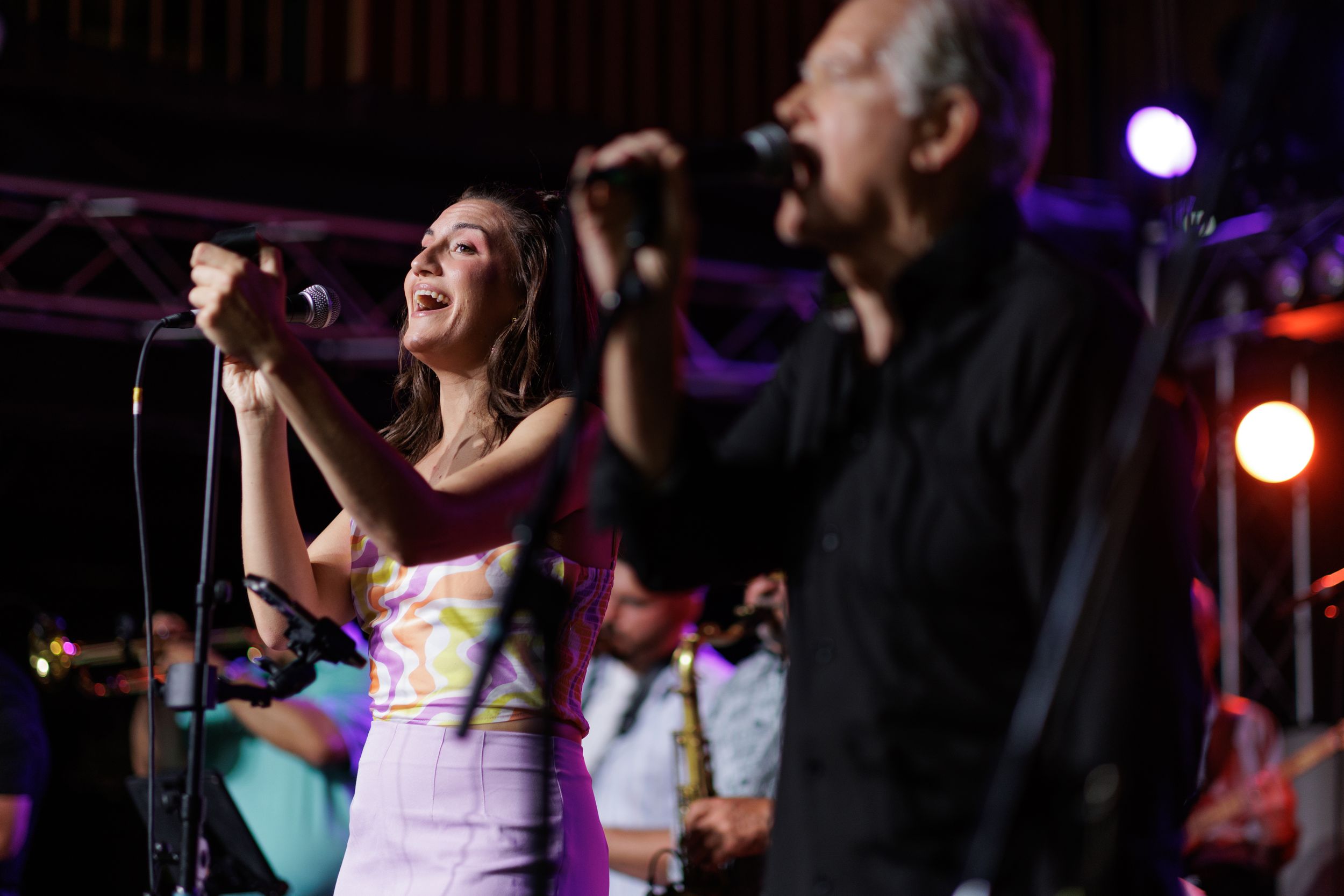 Two performers sing passionately into microphones on stage during a concert with dramatic lighting.