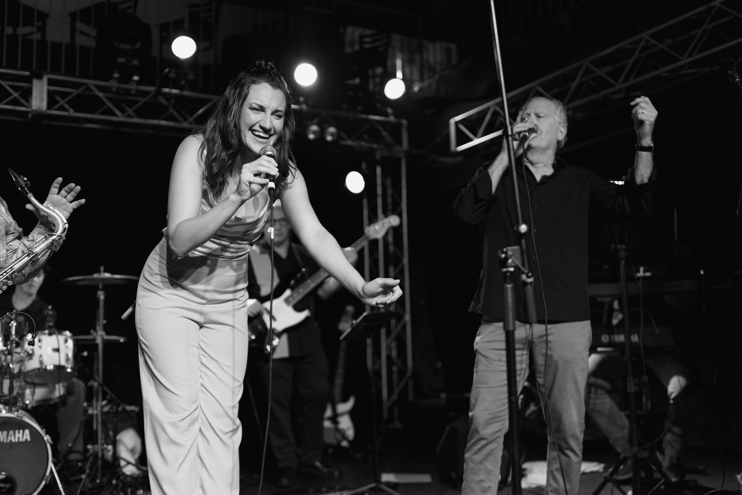 Black and white photo of two performers singing into microphones during an intimate live music performance.