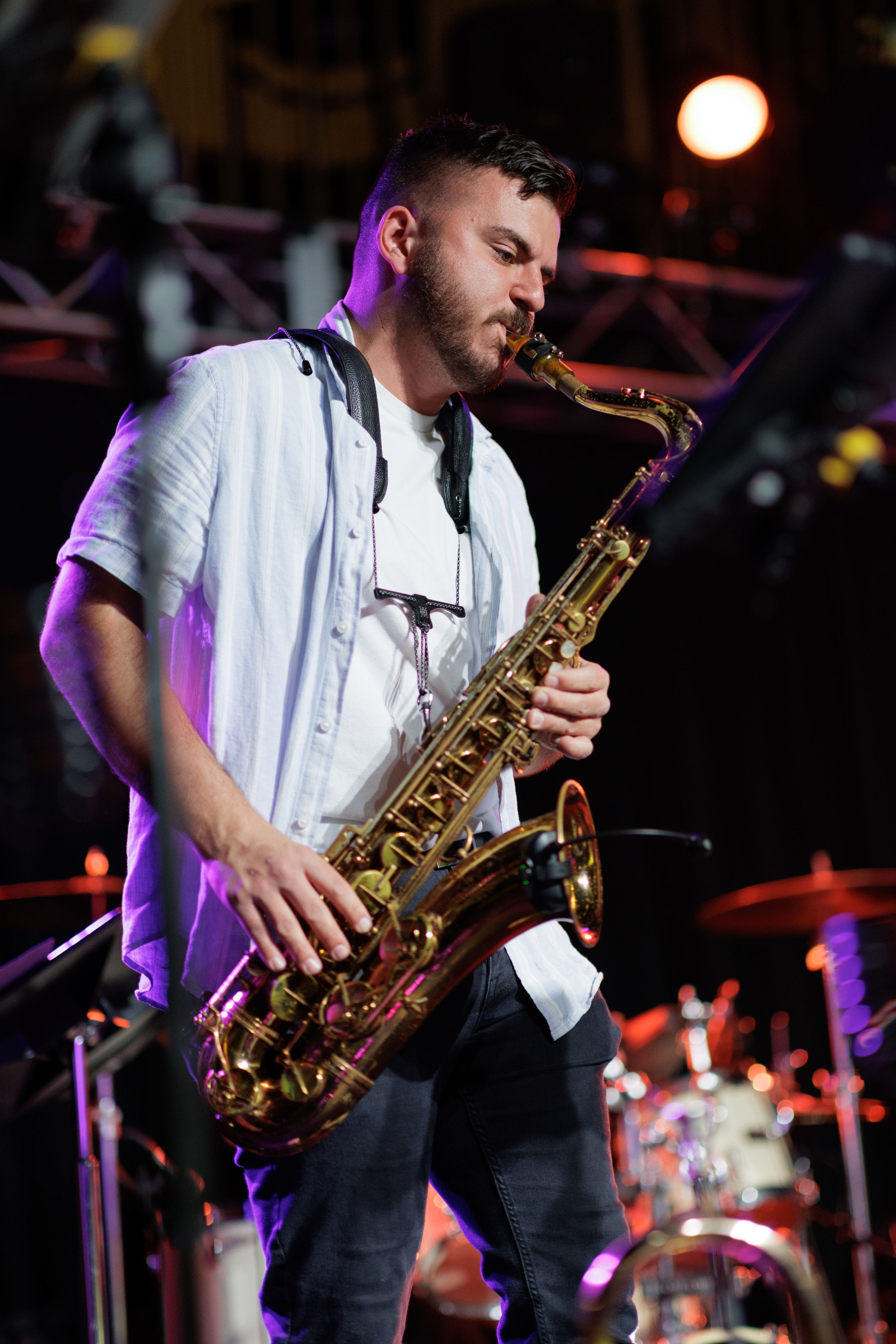 Musician performing on stage with saxophone under colorful purple lighting at live concert venue.