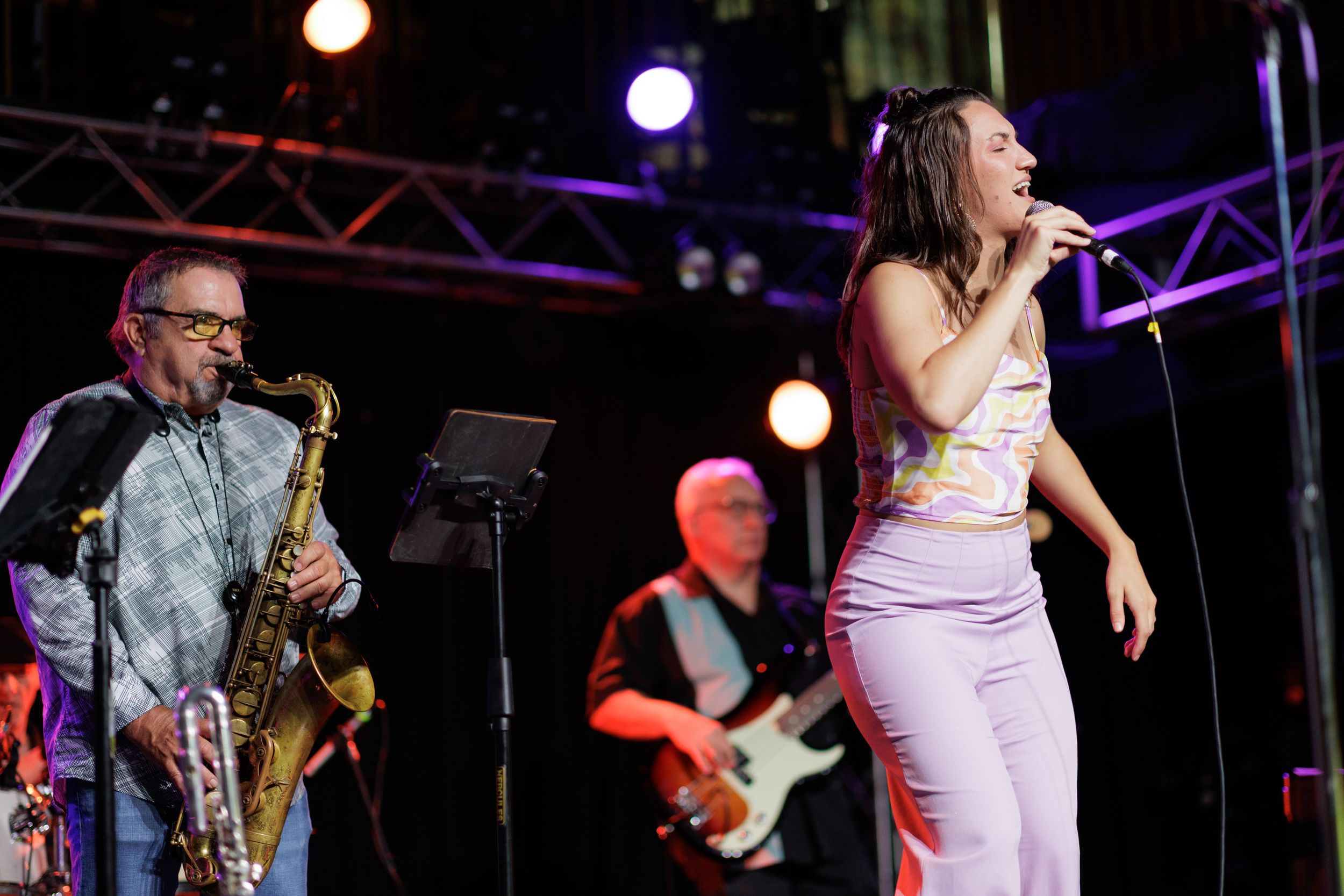 Saxophone player and vocalist perform on stage under dramatic concert lighting.