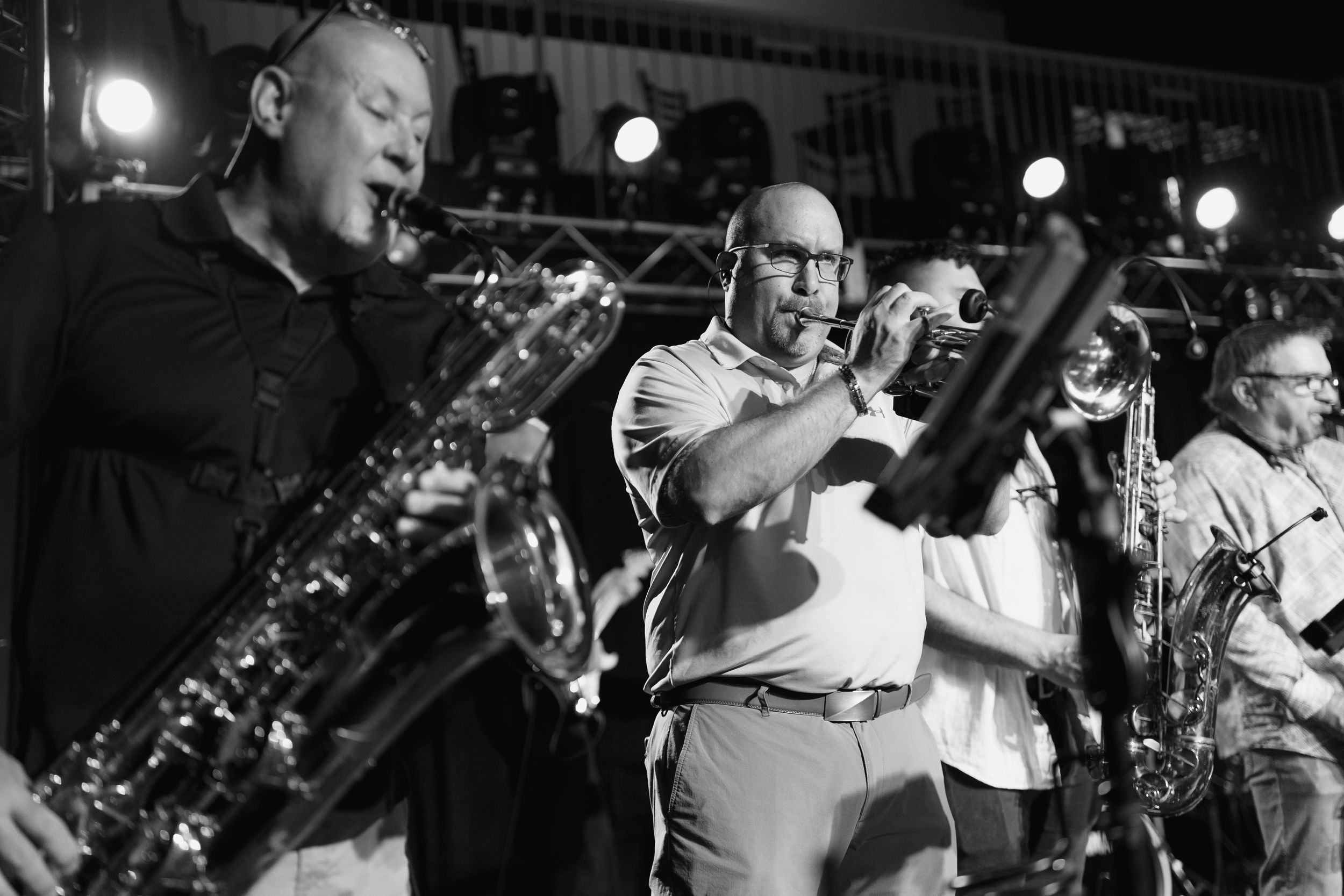 Black and white photo of horn players performing passionately on stage under bright spotlights.