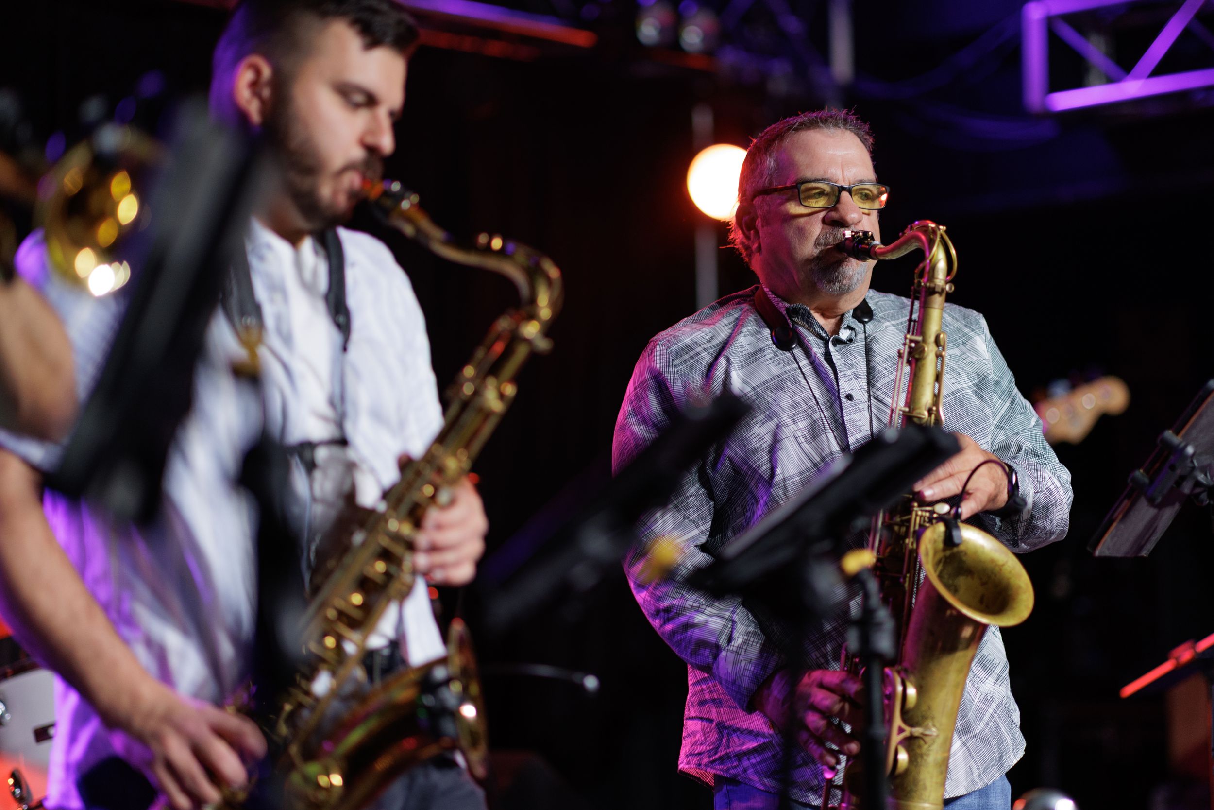 Several saxophonists perform together on stage under purple lighting during a jazz concert performance.