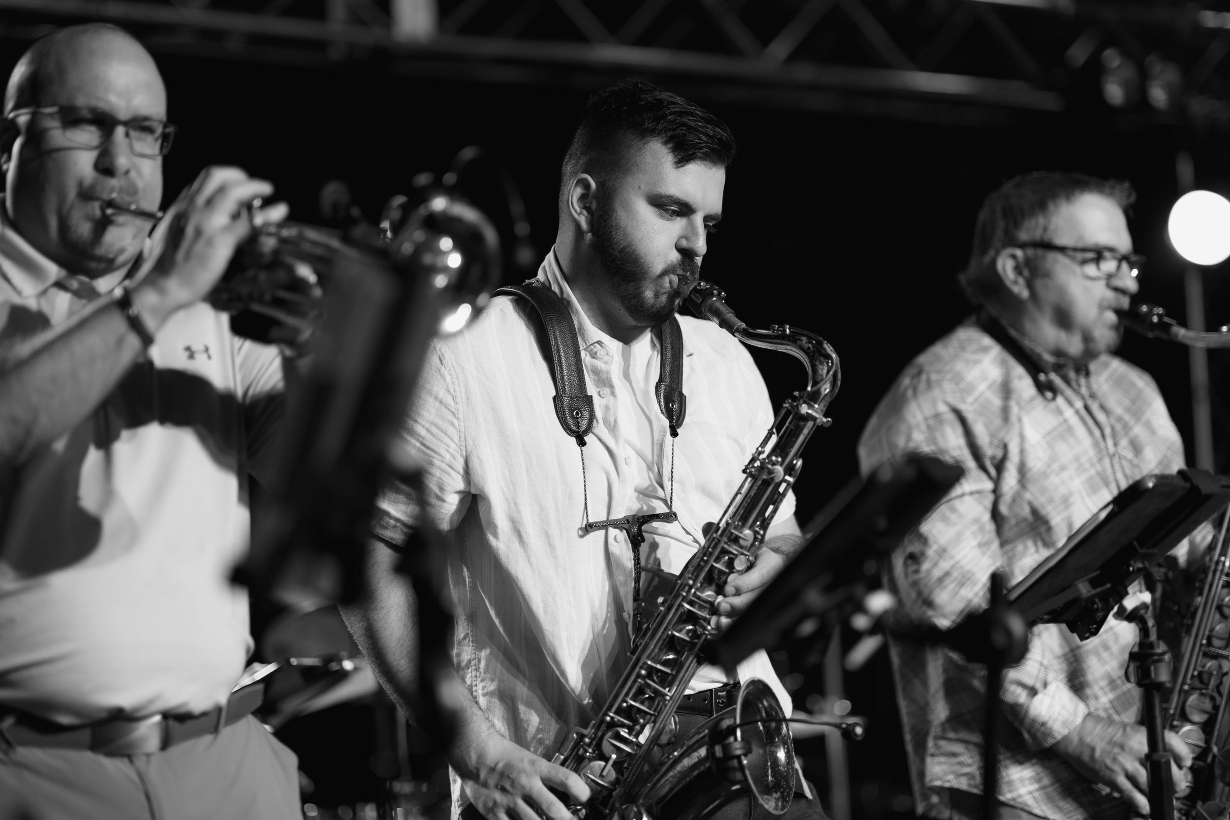 Black and white photo of a jazz ensemble performing with saxophone and other instruments on stage under moody lighting.
