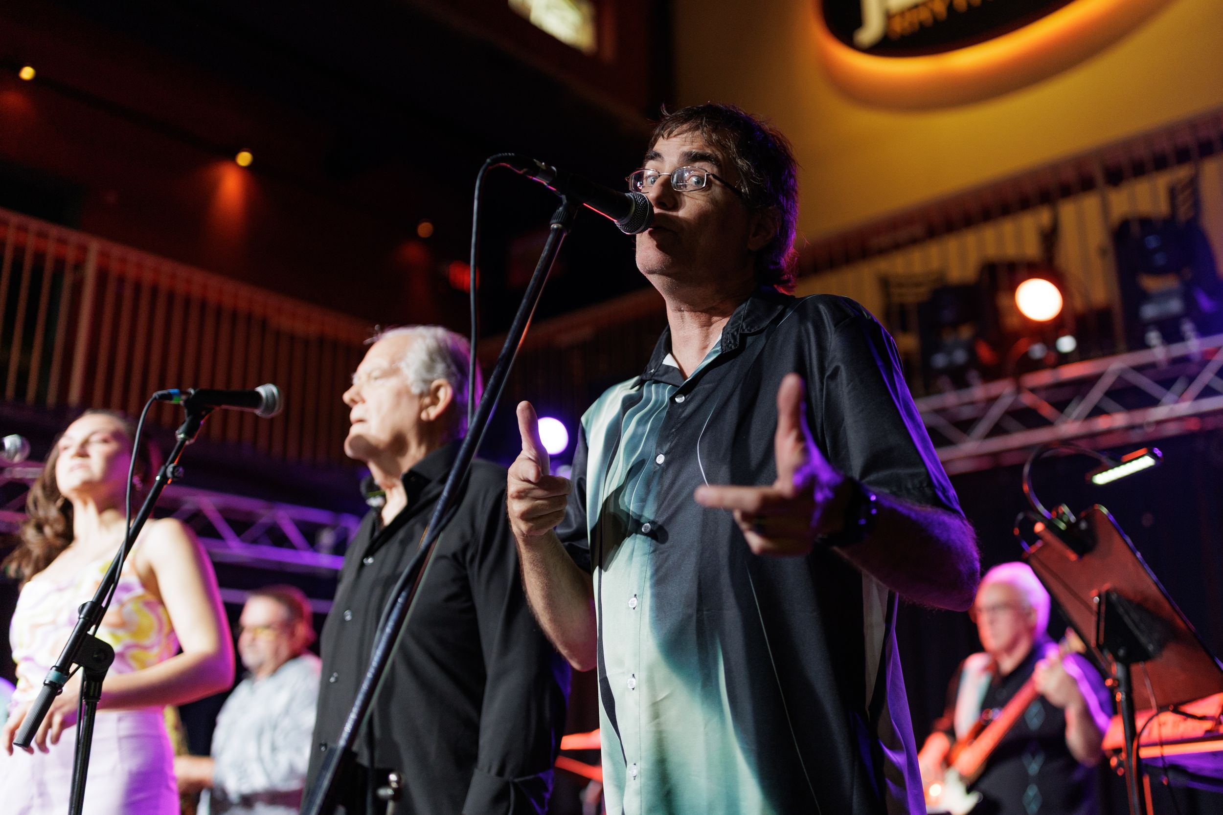 Musicians perform on stage at a lively concert with colorful lighting and energetic atmosphere.