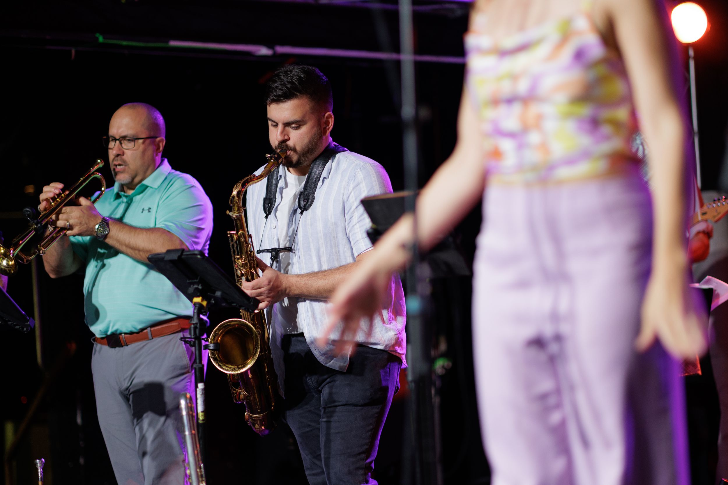 Musicians perform on stage with brass instruments and microphones during a live concert performance.