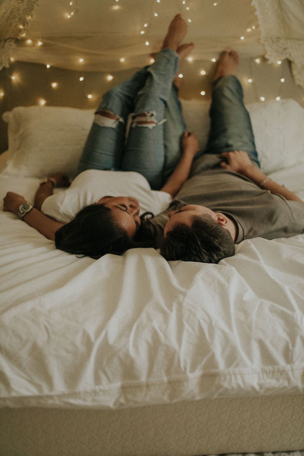 Couple relaxing on white bedding under twinkling fairy lights.