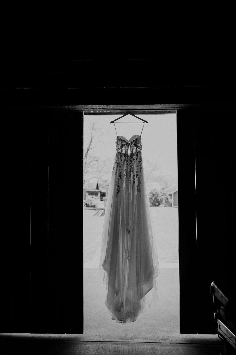 A wedding dress hangs elegantly against a white backdrop in a black and white photograph.