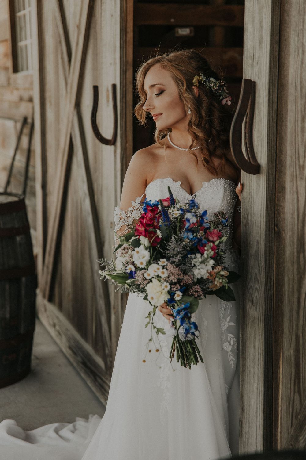 Bride holding a vibrant bouquet with blue and pink flowers against a rustic wooden backdrop.