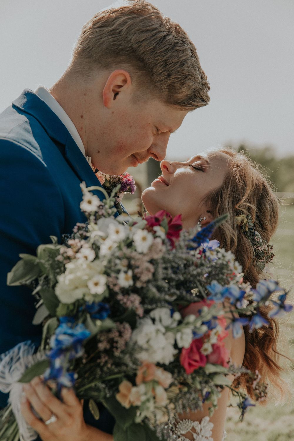 Romantic wedding couple embracing behind colorful floral bouquet outdoors.