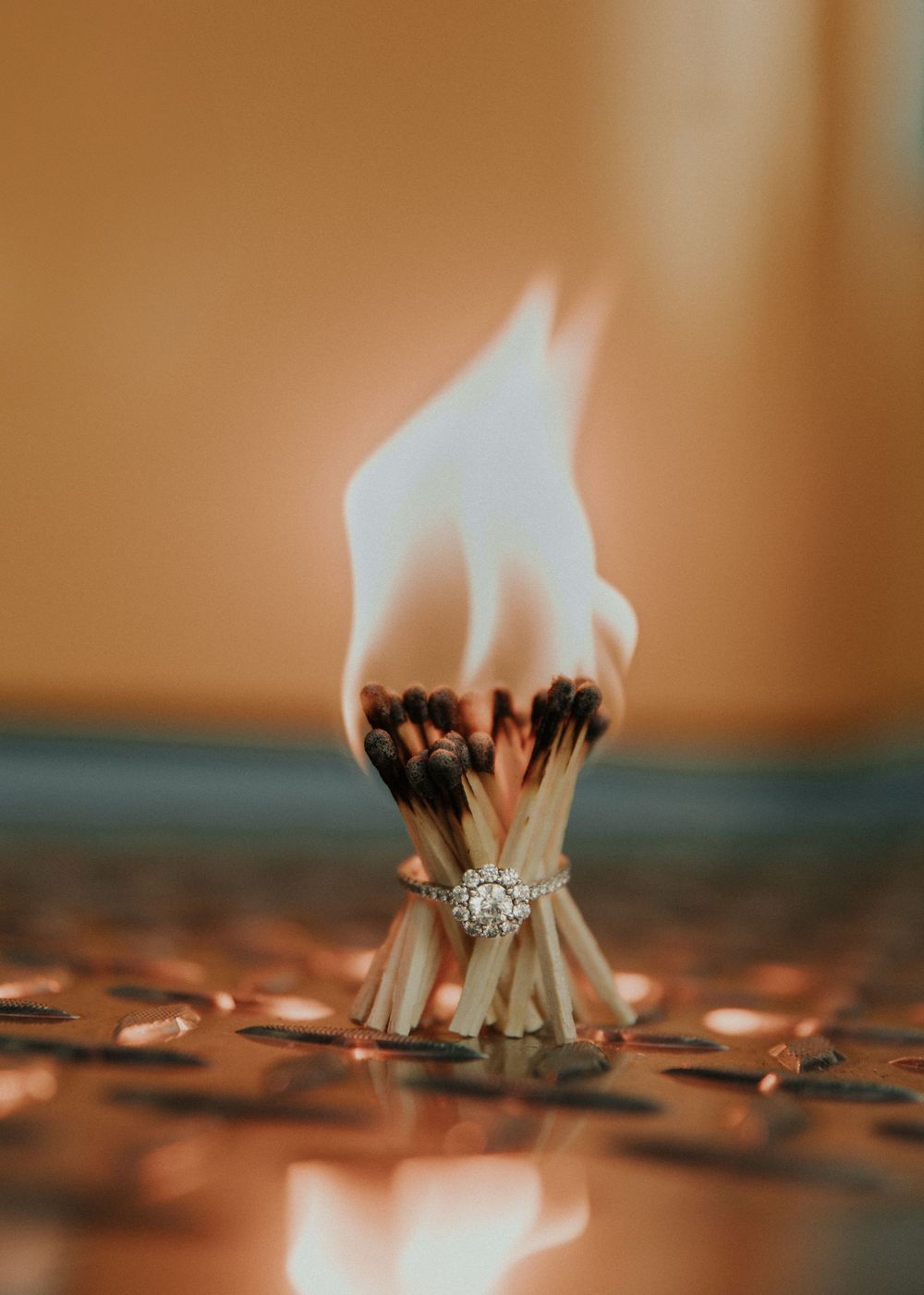 Close-up of diamond engagement ring with burning matches creating artistic reflection.
