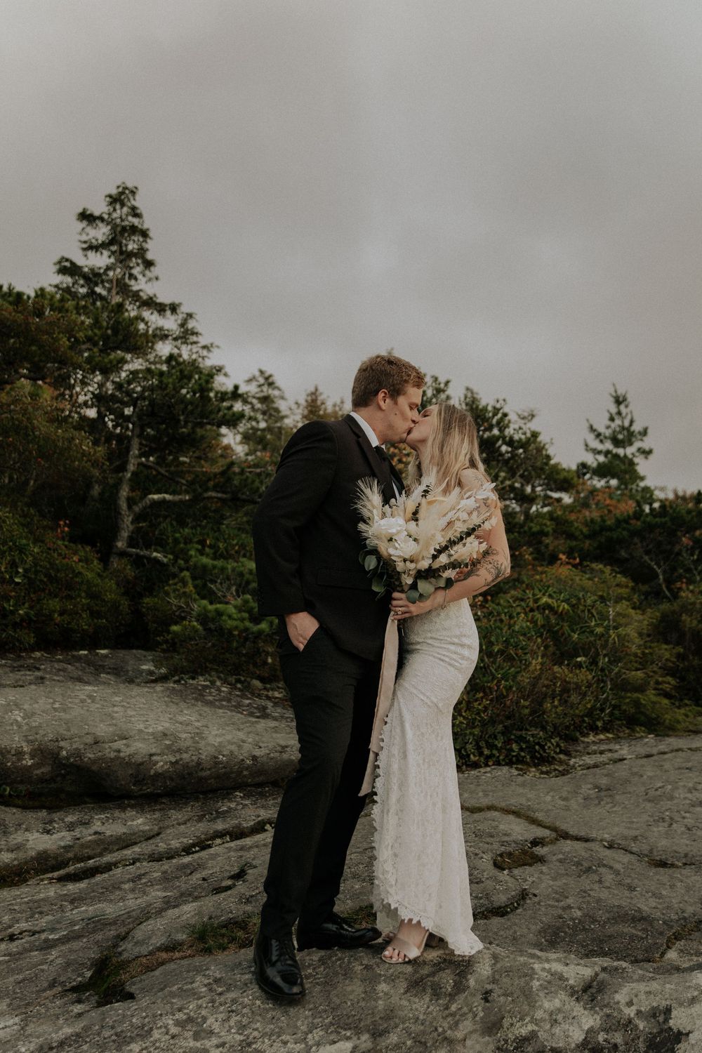 Couple sharing intimate moment on rocky outcrop against moody sky.