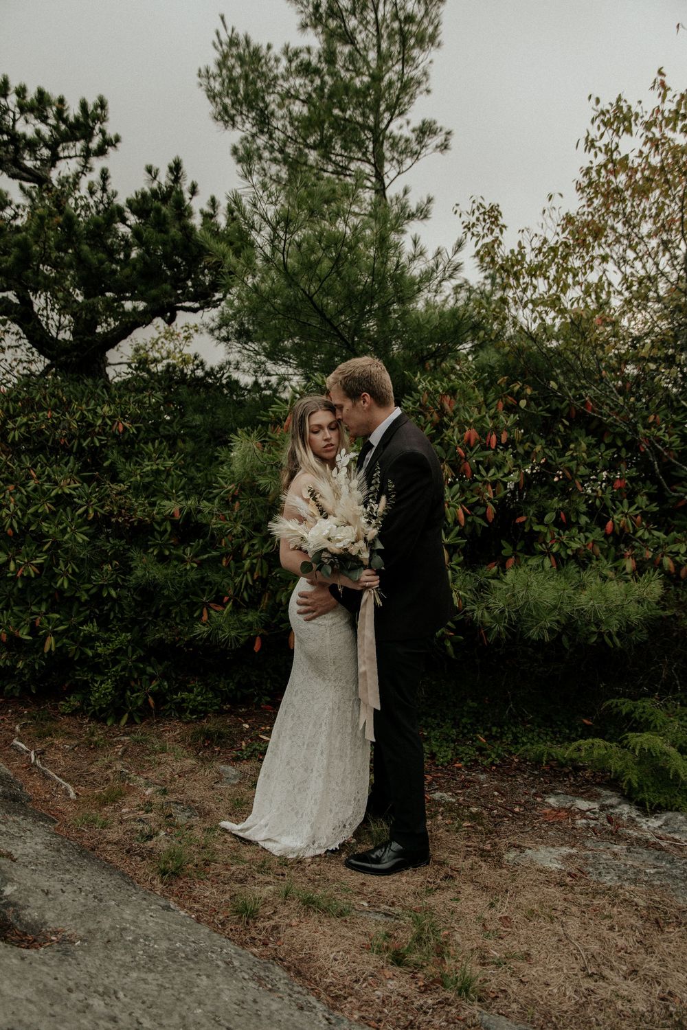 Wedding couple embracing on rocky terrain surrounded by autumn foliage.
