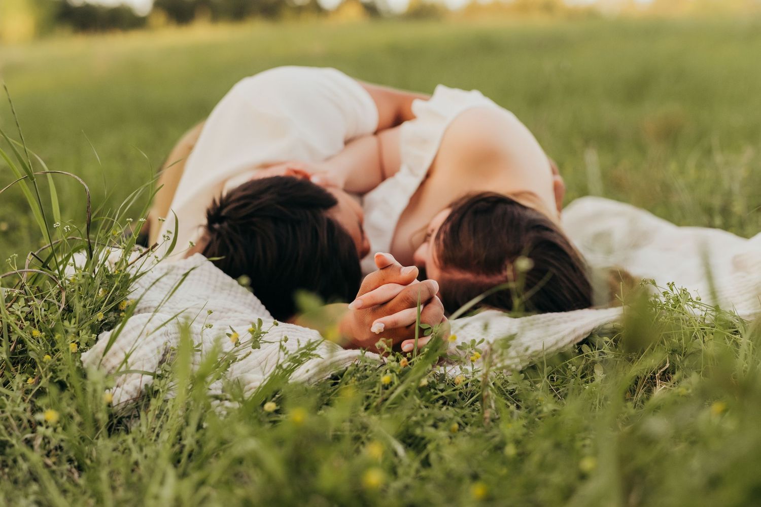 A couple in wedding attire lies together in a serene green meadow in Tyler, Tx during golden hour.