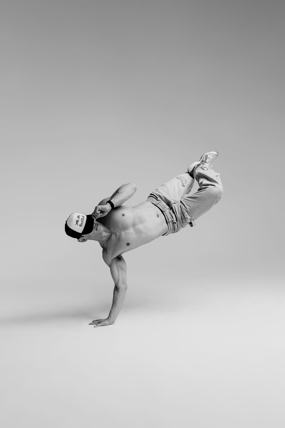 Athletic dancer performing a dynamic one-handed freeze breakdancing move in black and white against plain background.