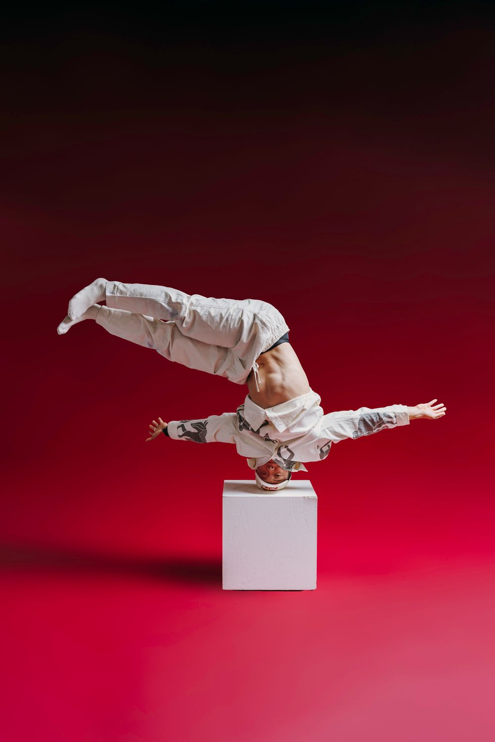 Artistic sequence showing a figure in white performing dynamic poses on a small white cube against a red backdrop.