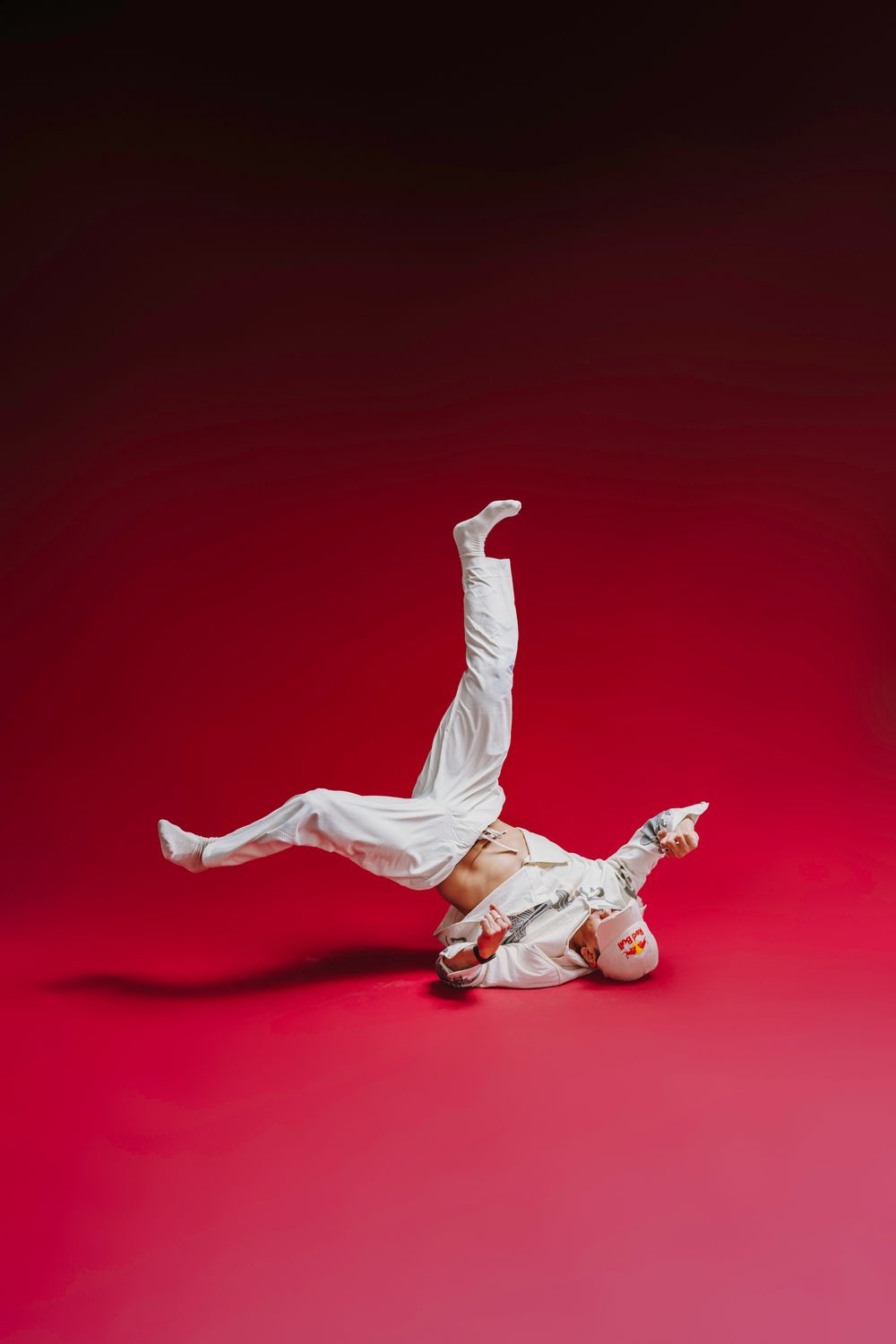 Athletic sequence of a performer in flowing white fabric doing acrobatic moves on red background.