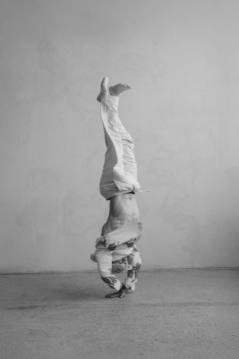 A performer in white clothing executes a dramatic headstand pose in black and white.