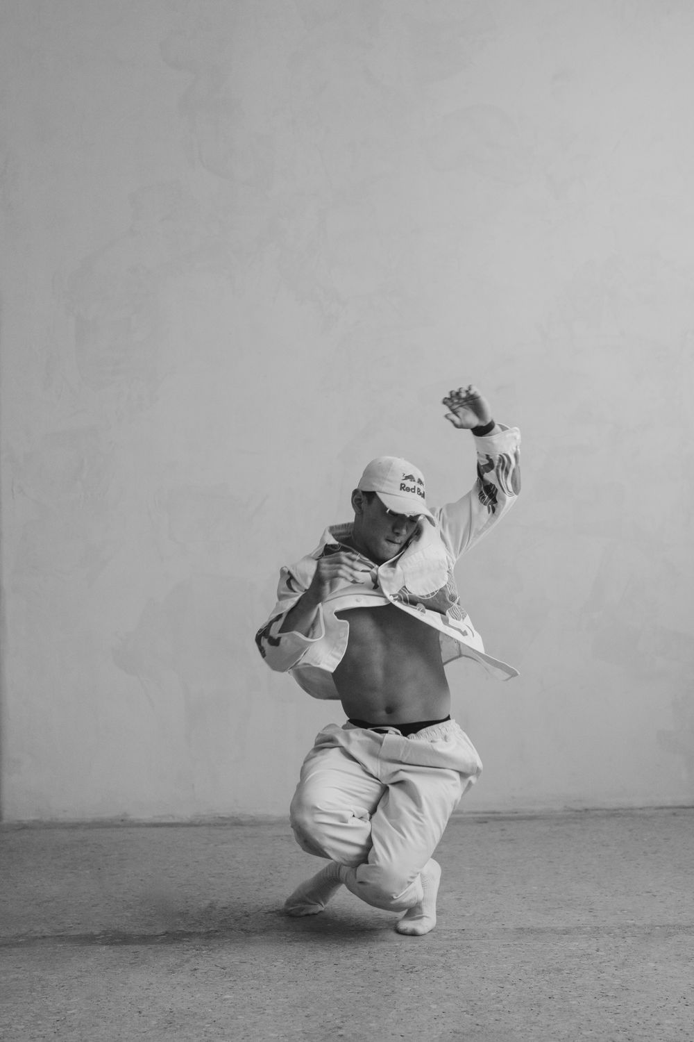 Black and white photo of a dancer in loose clothing performing a dramatic movement on a stark background.
