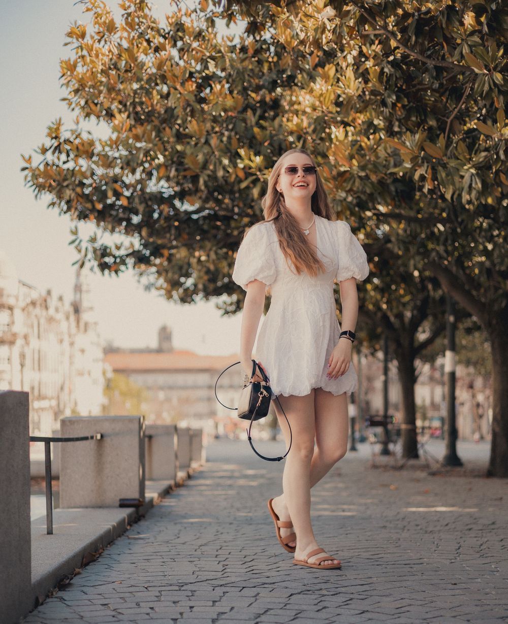 Woman in white summer dress walking along cobblestone path under autumn tree.