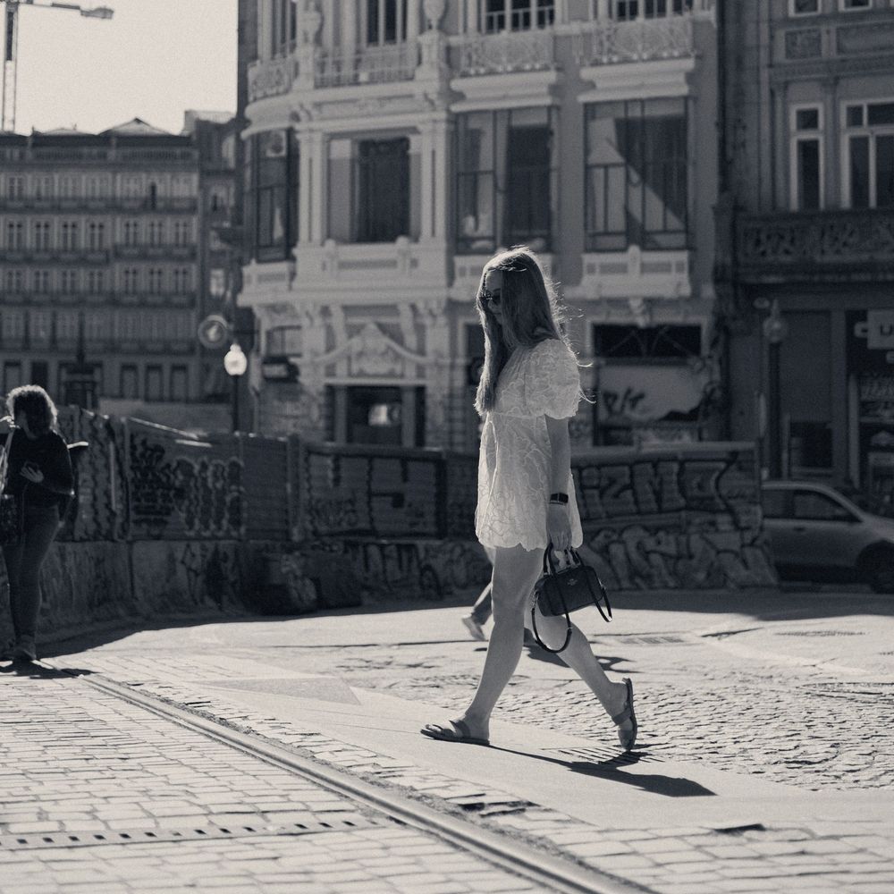 Black and white photo of person in white dress crossing urban street.