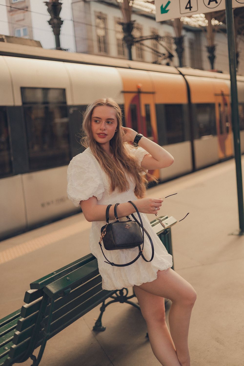 Woman in white dress posing by train platform with modern tram in background.