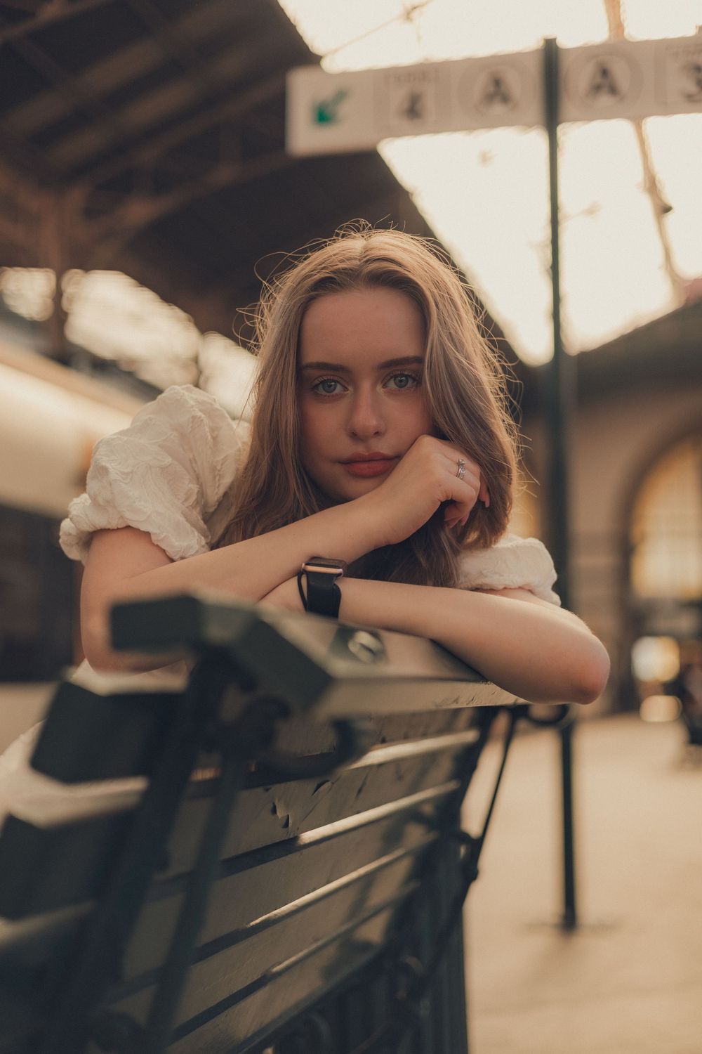 Vintage-style portrait at train station with directional signs overhead.