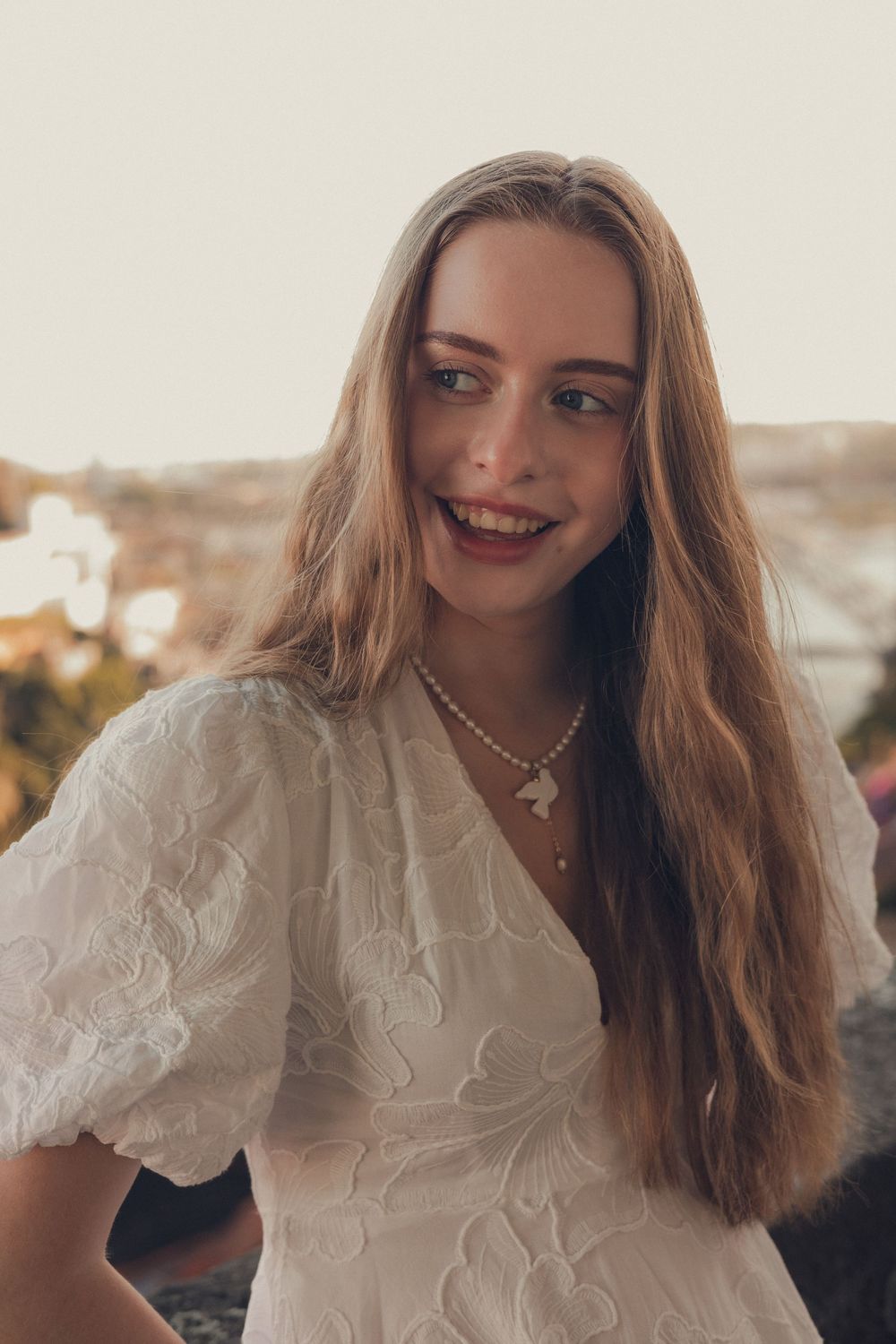 Elegant white lace dress with puff sleeves photographed against a warm sunset cityscape background.