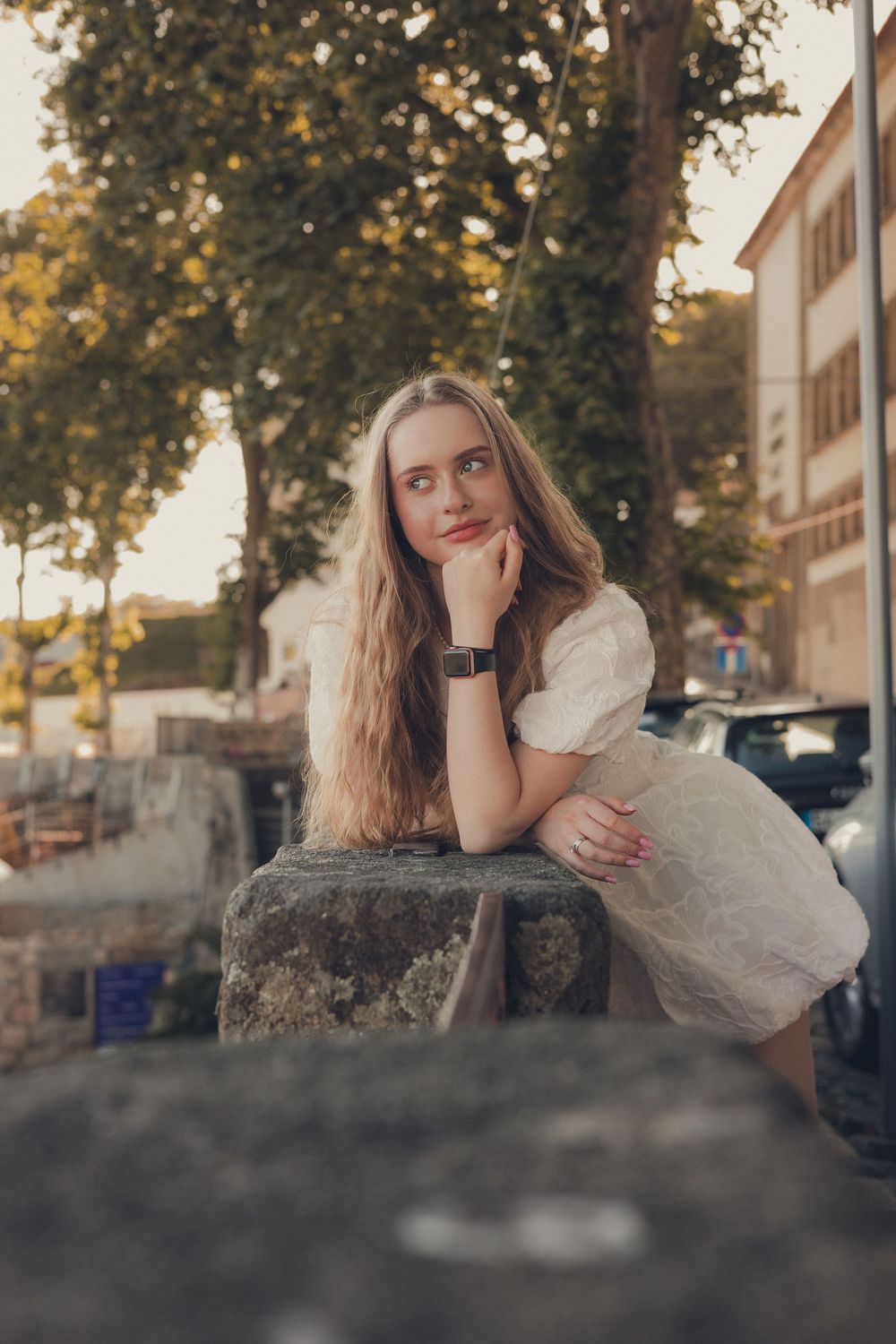 Romantic portrait featuring white dress and long hair against urban stone wall setting.