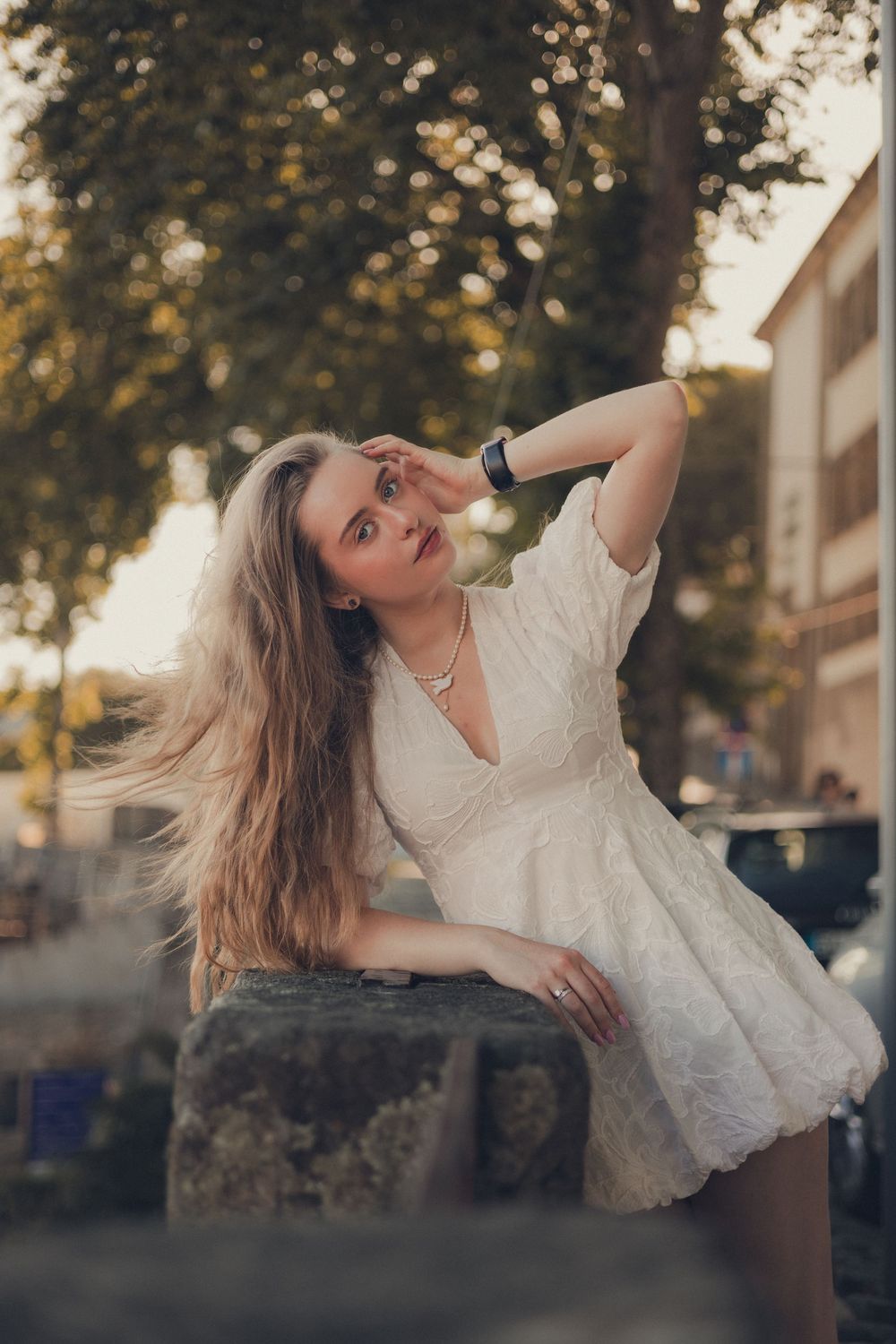 Carefree pose on stone wall wearing white lace mini dress with flowing hair.