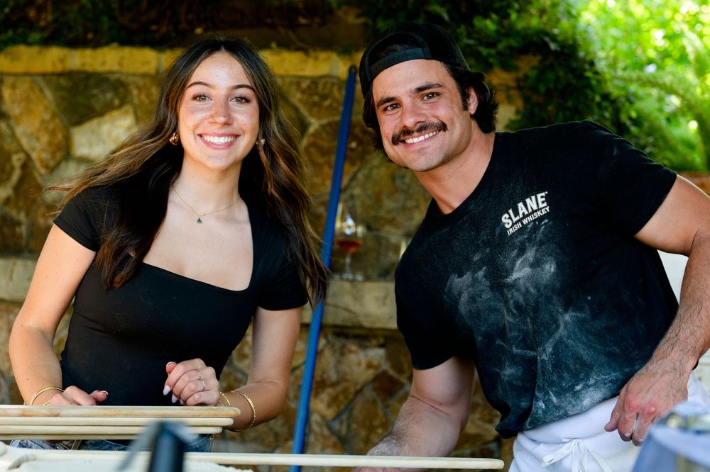 Two people pause making wood fired pizza to smile at a counter outdoors. Branding Sonoma, California - Lambert Bridge Winery