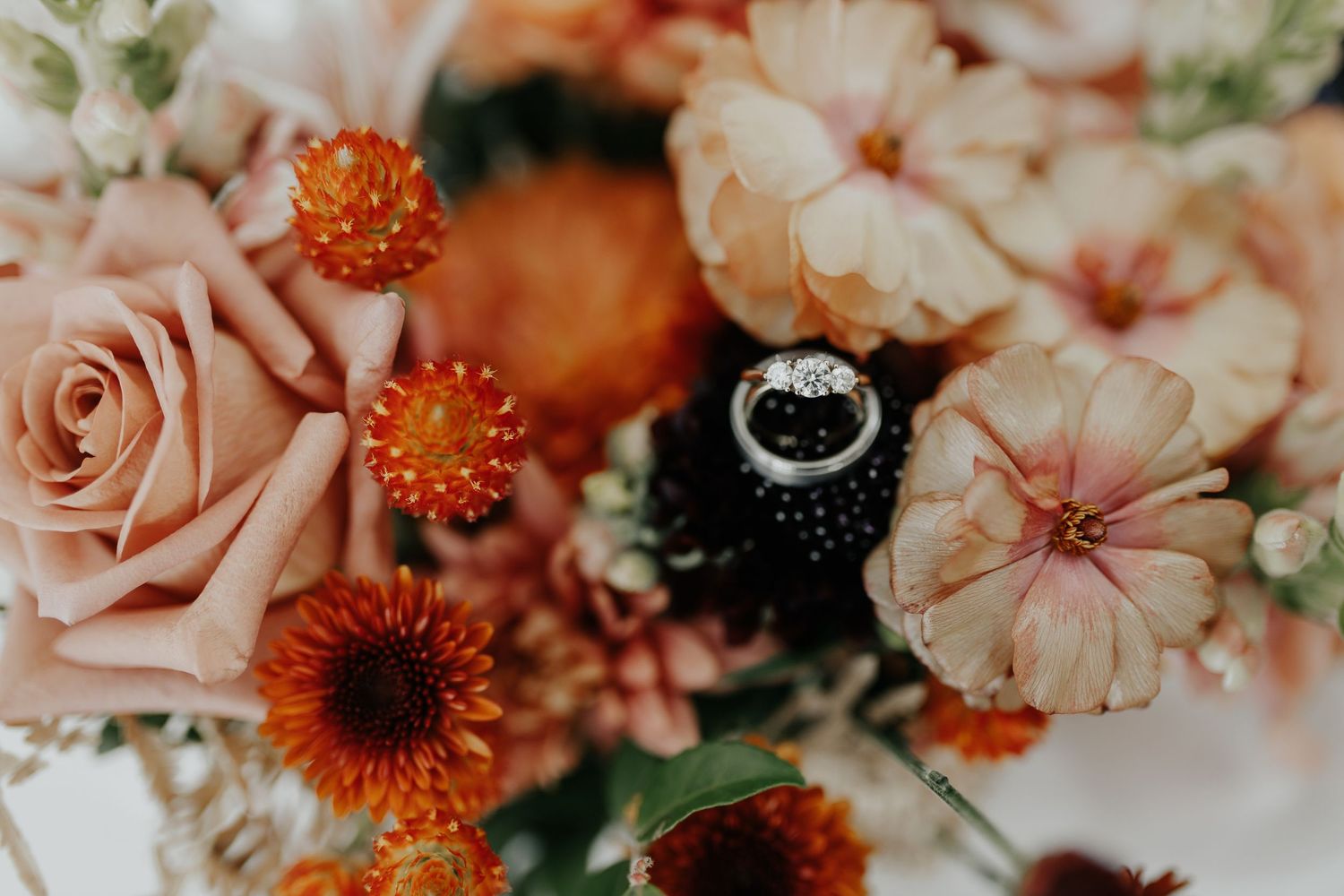 Wedding rings placed elegantly on white anemone and ranunculus flowers in a bridal bouquet.
