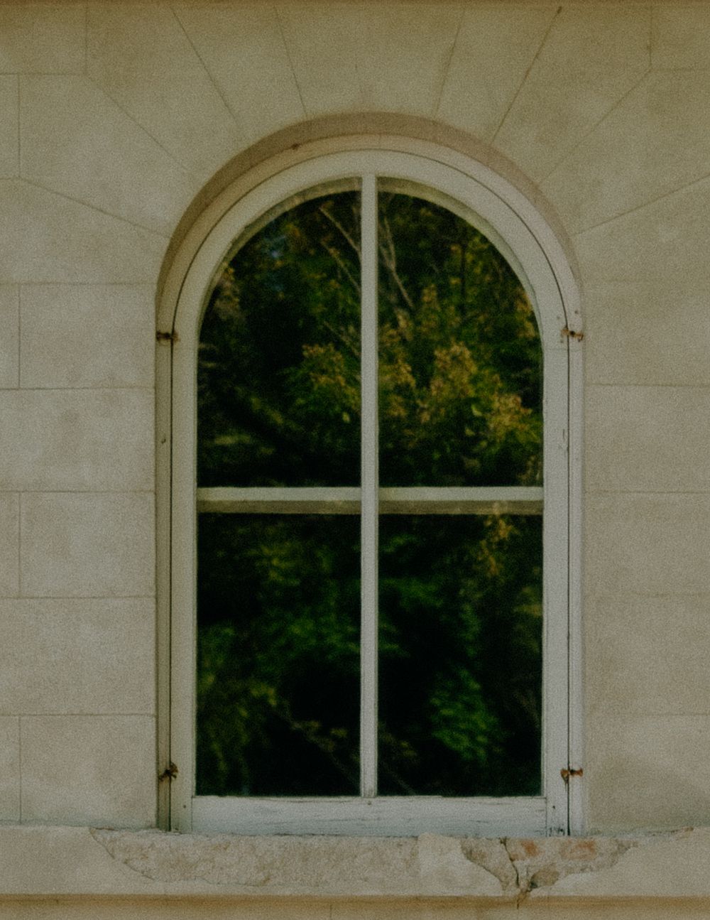 Series of three arched windows on a white stone wall with greenery visible through the glass panes.