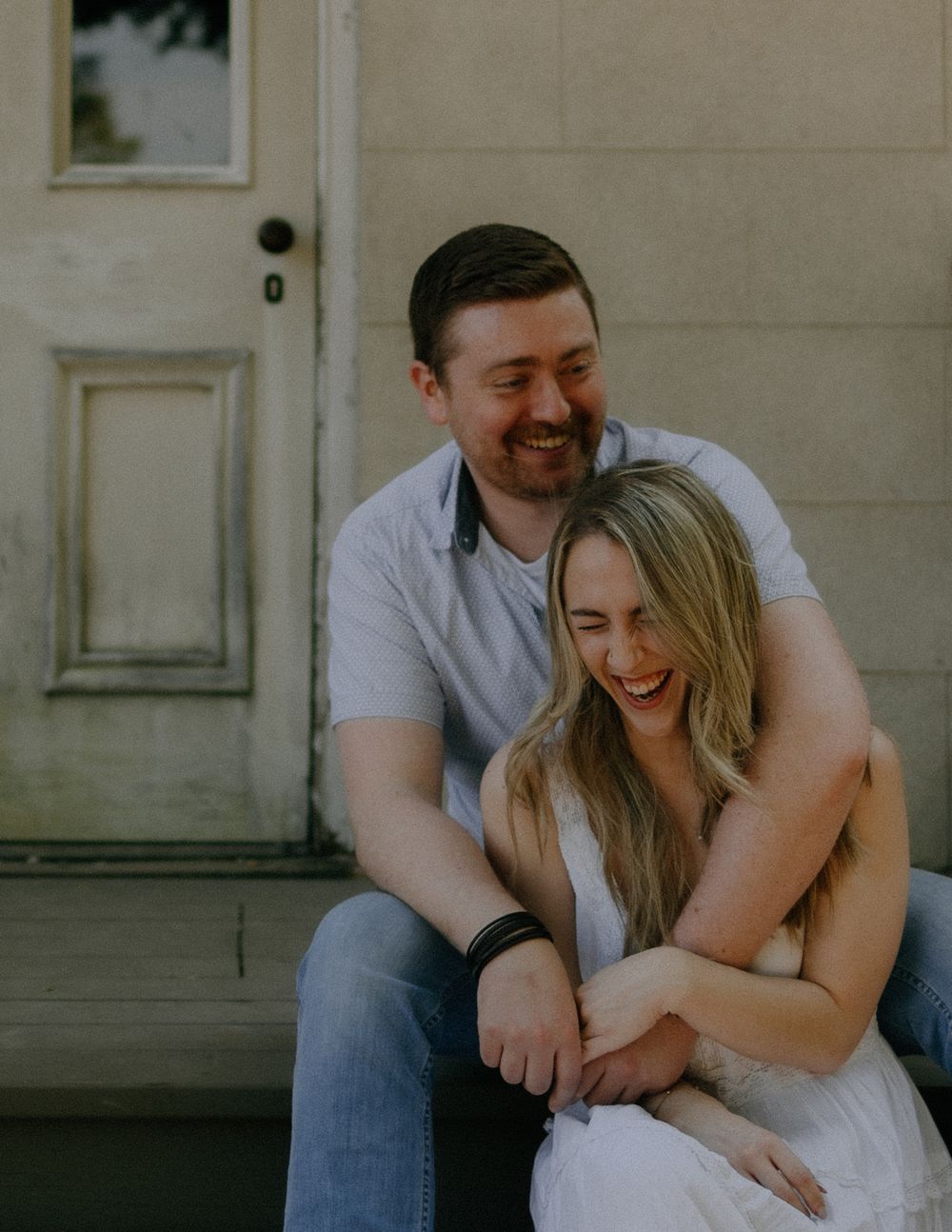 Happy couple sharing intimate moments together while sitting on steps outside a white building.