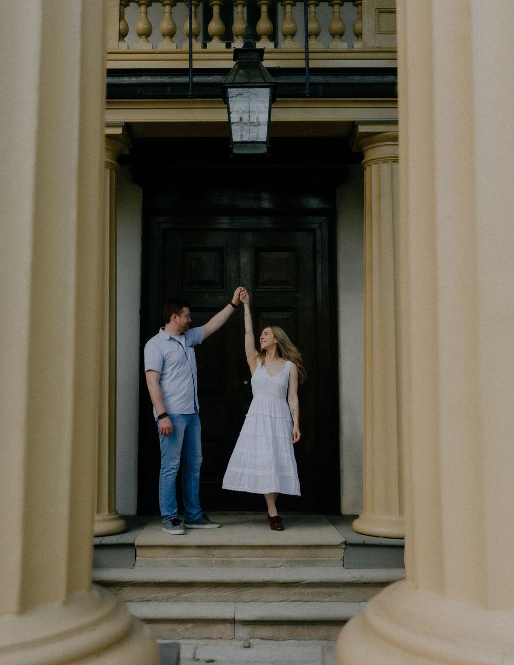 Couple embraces in an elegant architectural setting with white pillars and arches providing a romantic backdrop.