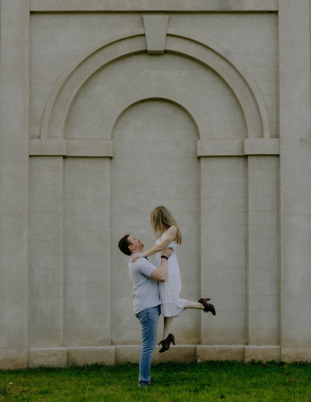 Romantic couple embracing in front of a white arched wall with architectural details in a minimalist outdoor setting.