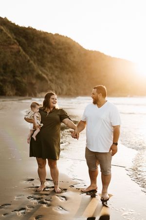 A family plays and laughs together on a beach at sunset.