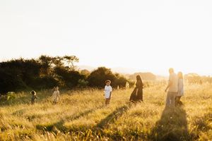 Silhouettes of people walking through tall grass field at sunset.