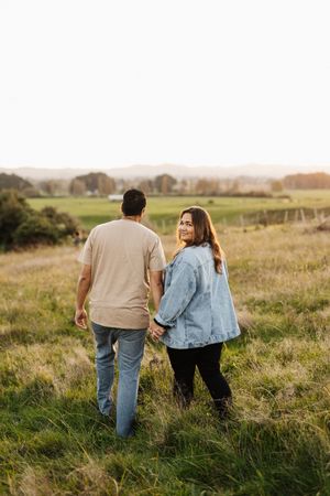 Couple walking hand in hand through a grassy hillside at sunset.