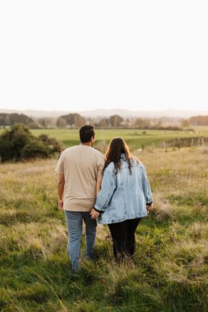 Couple in casual wear walking together on a hilltop during golden hour.