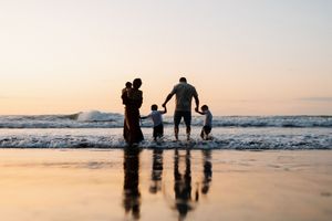 Silhouettes of a family walking along the beach at sunset with waves rolling in.