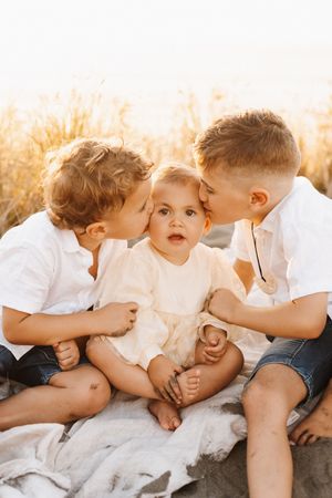 Children lay close together on a blanket, sharing playful moments in warm sunlight.