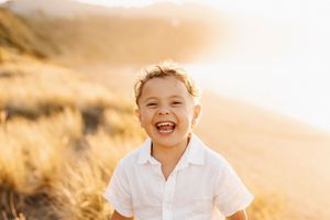 A child laughs joyfully in the golden sunset light amidst tall grass.